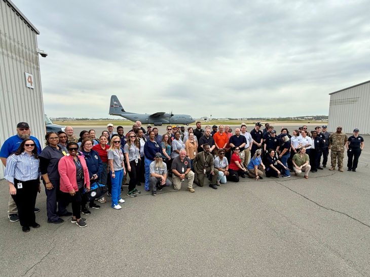 Large crowd of people pose for photo at airport during exercise.